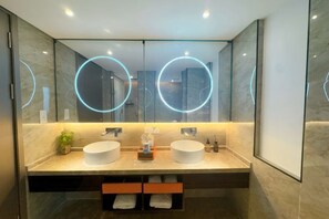 Un baño moderno con dos lavamanos, paredes espejadas e iluminación circular.