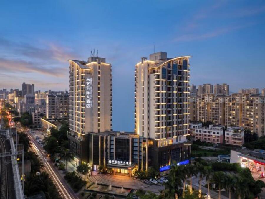 Un edificio de gran altura con varios pisos, rodeado de otros edificios y una calle concurrida llena de vehículos.