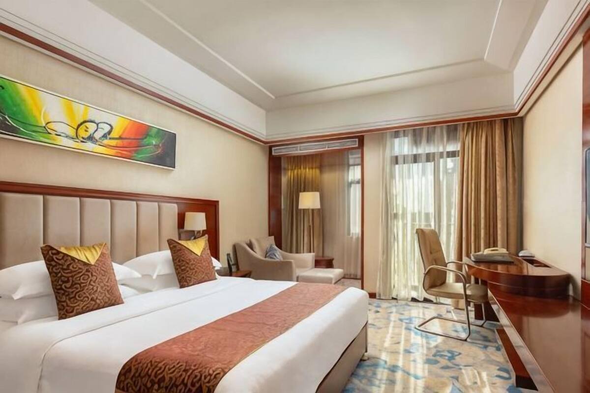Ein Hotelzimmer mit einem großen Bett, einem Schreibtisch, einem Stuhl, einer Lampe und einem Bild an der Wand.