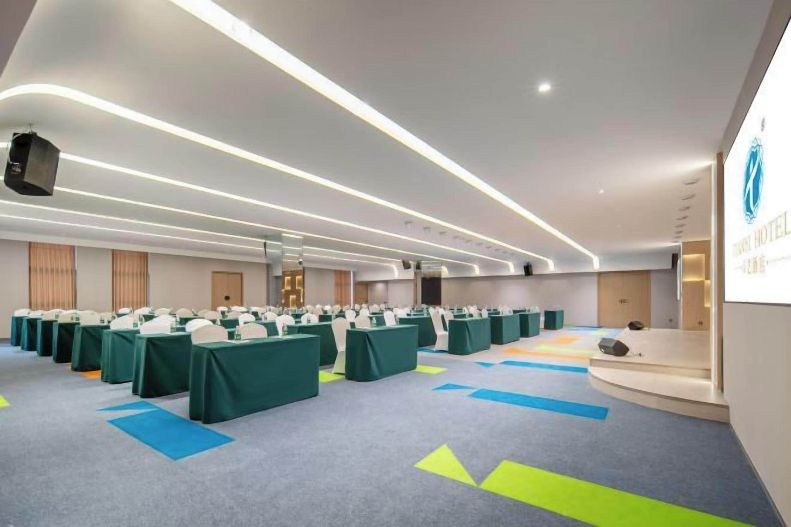 Un salón de conferencias con filas de mesas, un escenario y una mesa de recepción.