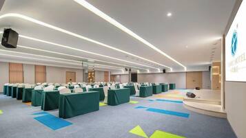 Un salón de conferencias con filas de mesas, un escenario y una mesa de recepción.