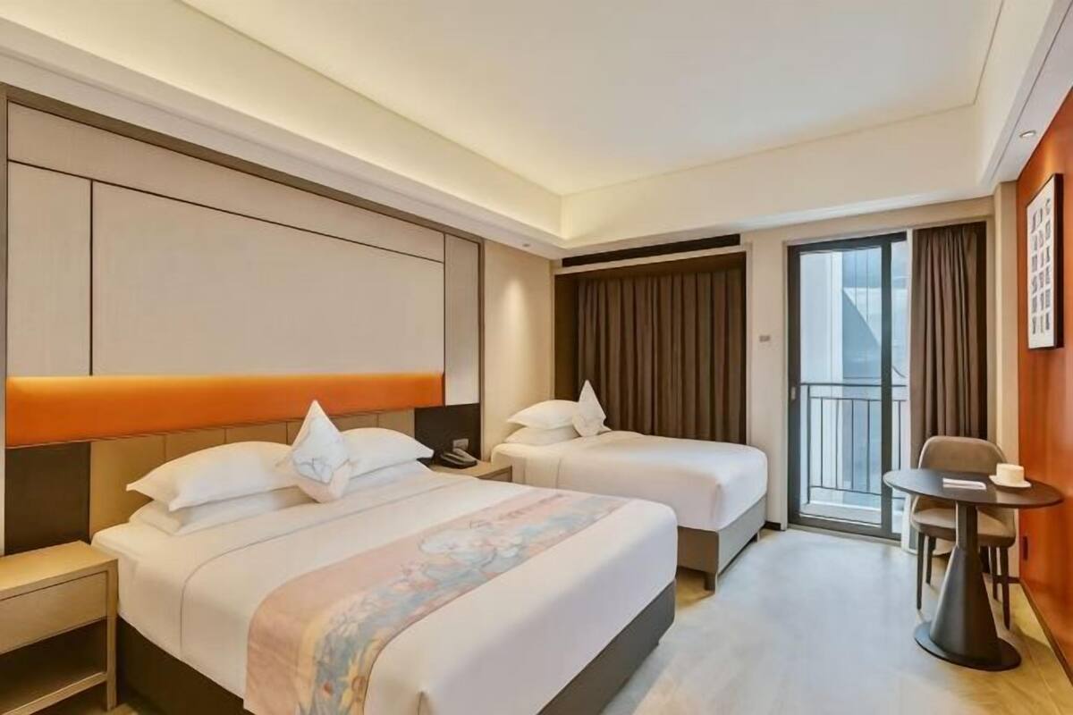 Ein Hotelzimmer mit zwei Betten, einem kleinen Tisch, einem Stuhl, einem Balkon und einem großen Fenster.