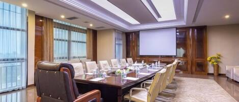 A conference room with a long table, chairs, a projector screen, and a large window.