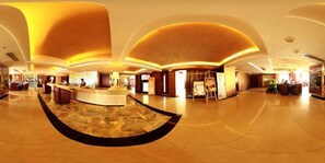 Un hall espacioso con un mostrador de recepción curvo, suelo de mármol y un diseño de techo moderno.