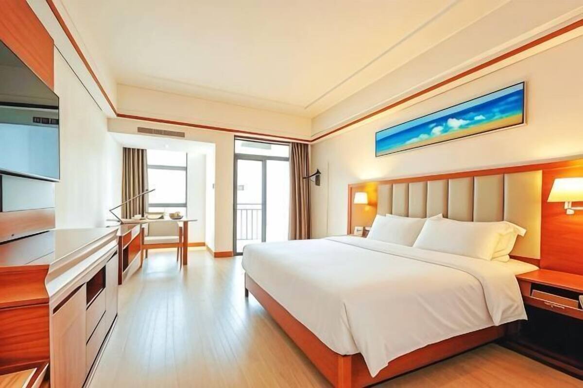 Ein Hotelzimmer mit Bett, Schreibtisch, Stuhl, Fernseher und einem Bild an der Wand.