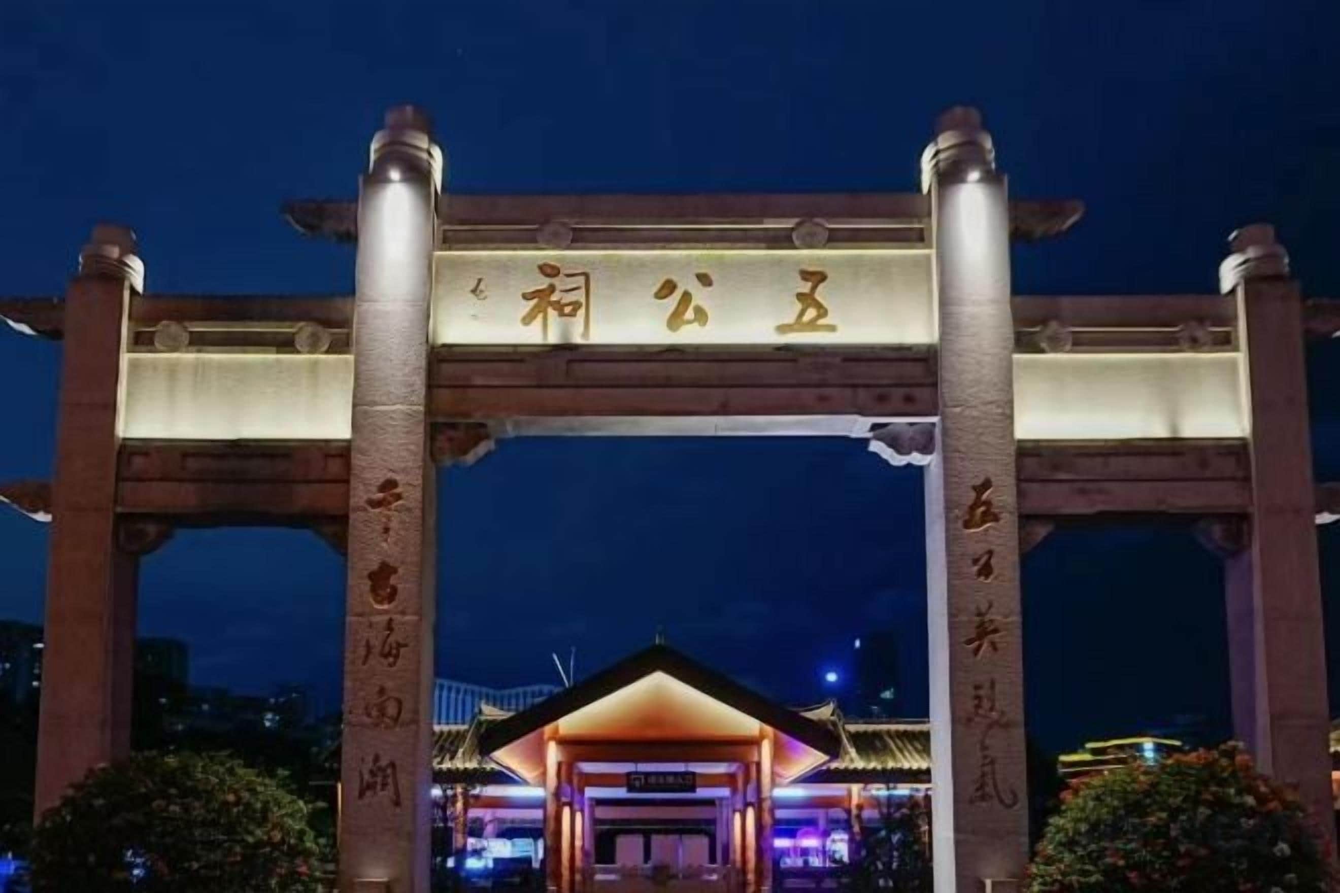 A traditional Japanese torii gate with illuminated characters, leading to a building with a pagoda-style roof.