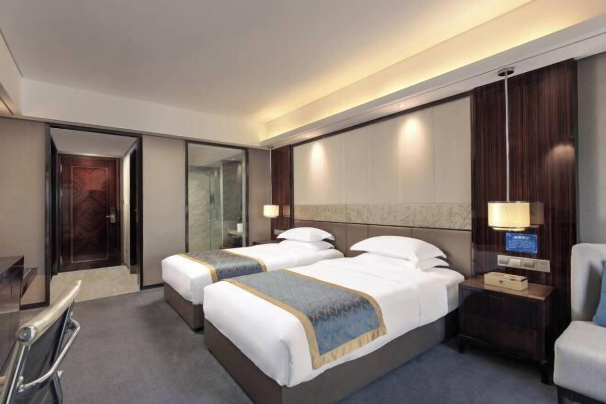 Ein Hotelzimmer mit zwei Betten, einem Schreibtisch, einem Sessel, einem Nachttisch und einem Spiegel.