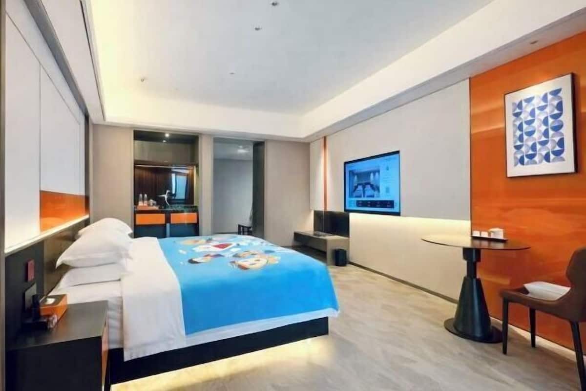 Ein modernes Hotelzimmer mit Bett, Schreibtisch, Sessel, Fernseher und einem kleinen Tisch.