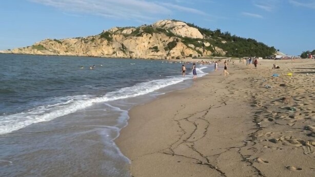 Ein Strand mit Menschen, ein felsiger Hügel im Hintergrund und der Ozean.