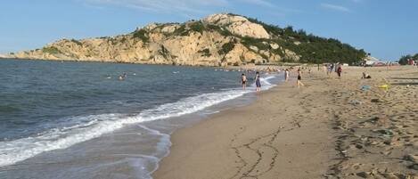 Una playa con un afloramiento rocoso al fondo, orilla arenosa e huellas.