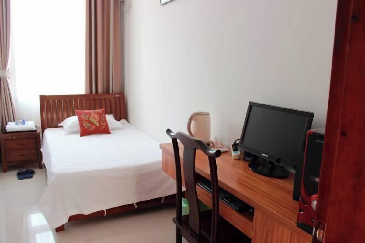 A hotel room with a bed, a desk with a computer, a chair, and a window with curtains.