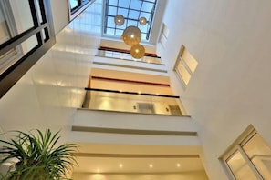 A multi-level interior with a staircase, glass railings, and pendant lighting.