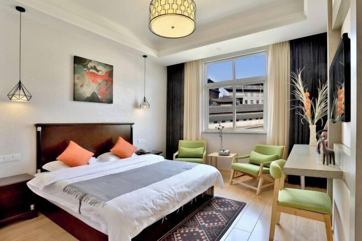 A hotel room with a bed, a desk, two chairs, a window with a view, and a painting on the wall.