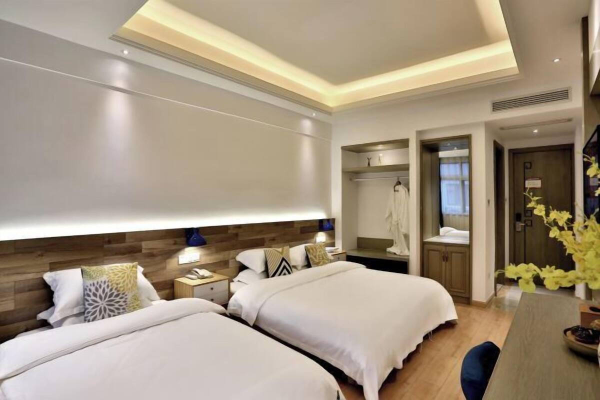 A hotel room with two beds, a wooden headboard, a desk with a chair, and a mirror.