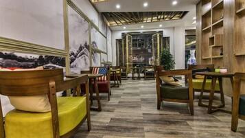 A hotel lobby with wooden furniture, a patterned floor, and a view into the dining area.