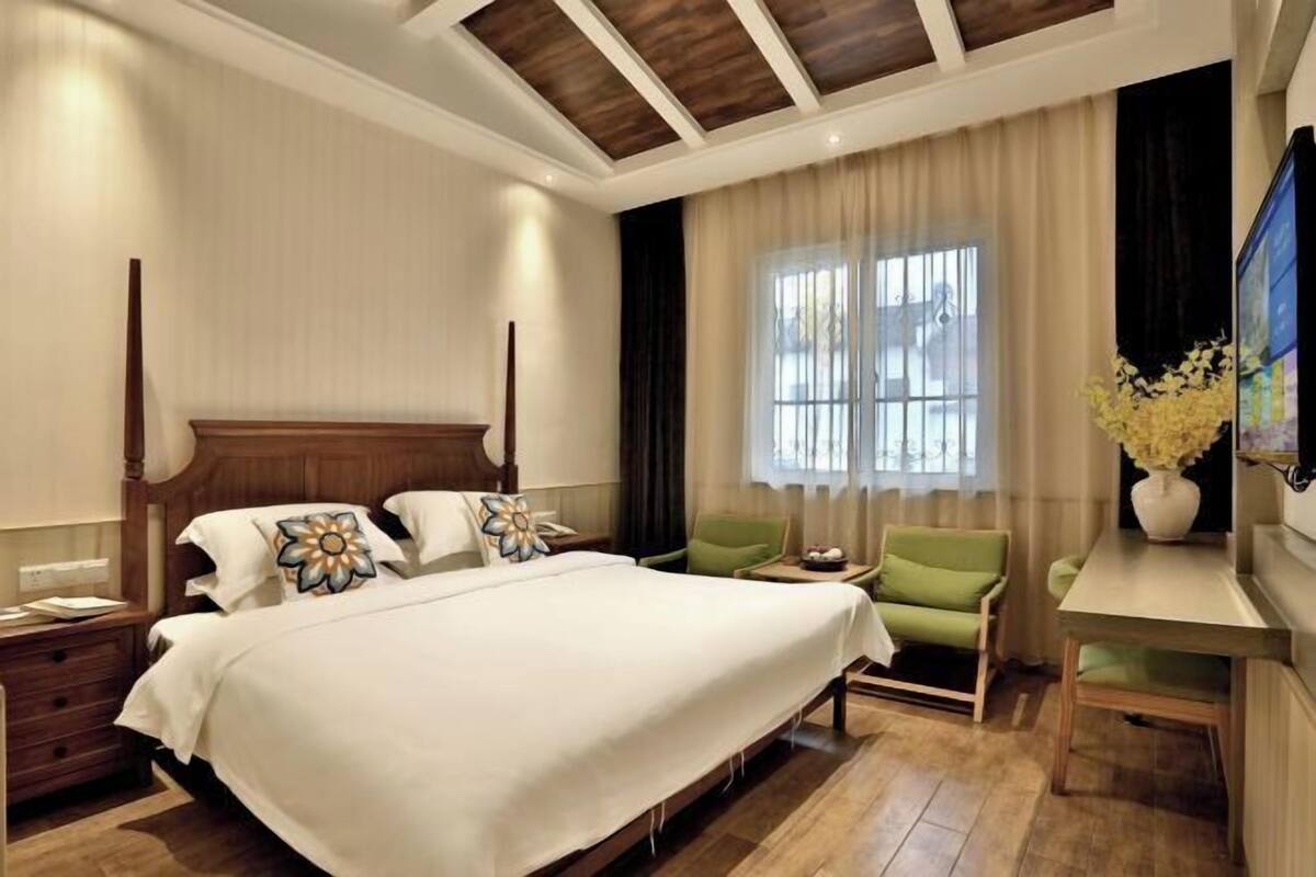 A hotel room with a large bed, a desk, a chair, a nightstand, and a TV.