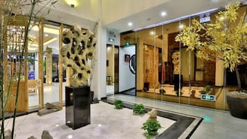 A lobby with a modern design, featuring a central sculpture, a glass storefront, and indoor plants.