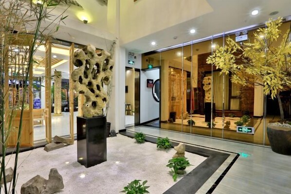 A lobby with a modern design, featuring a central sculpture, a glass storefront, and indoor plants.