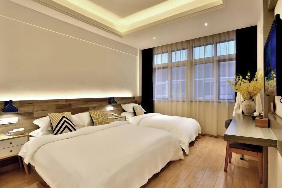 A hotel room with two beds, a desk, and a large window with curtains.