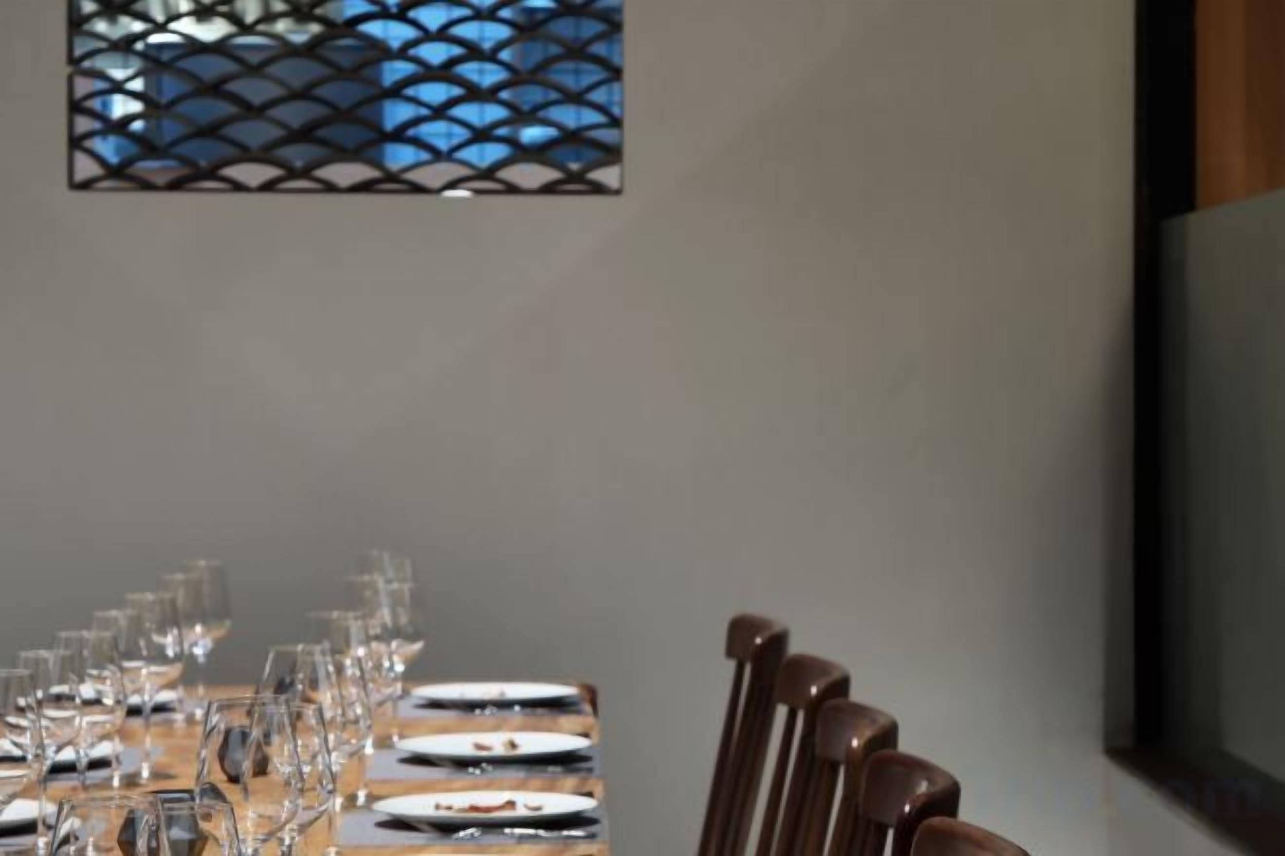 A dining table set with plates, glasses, and cutlery, with chairs positioned around it.