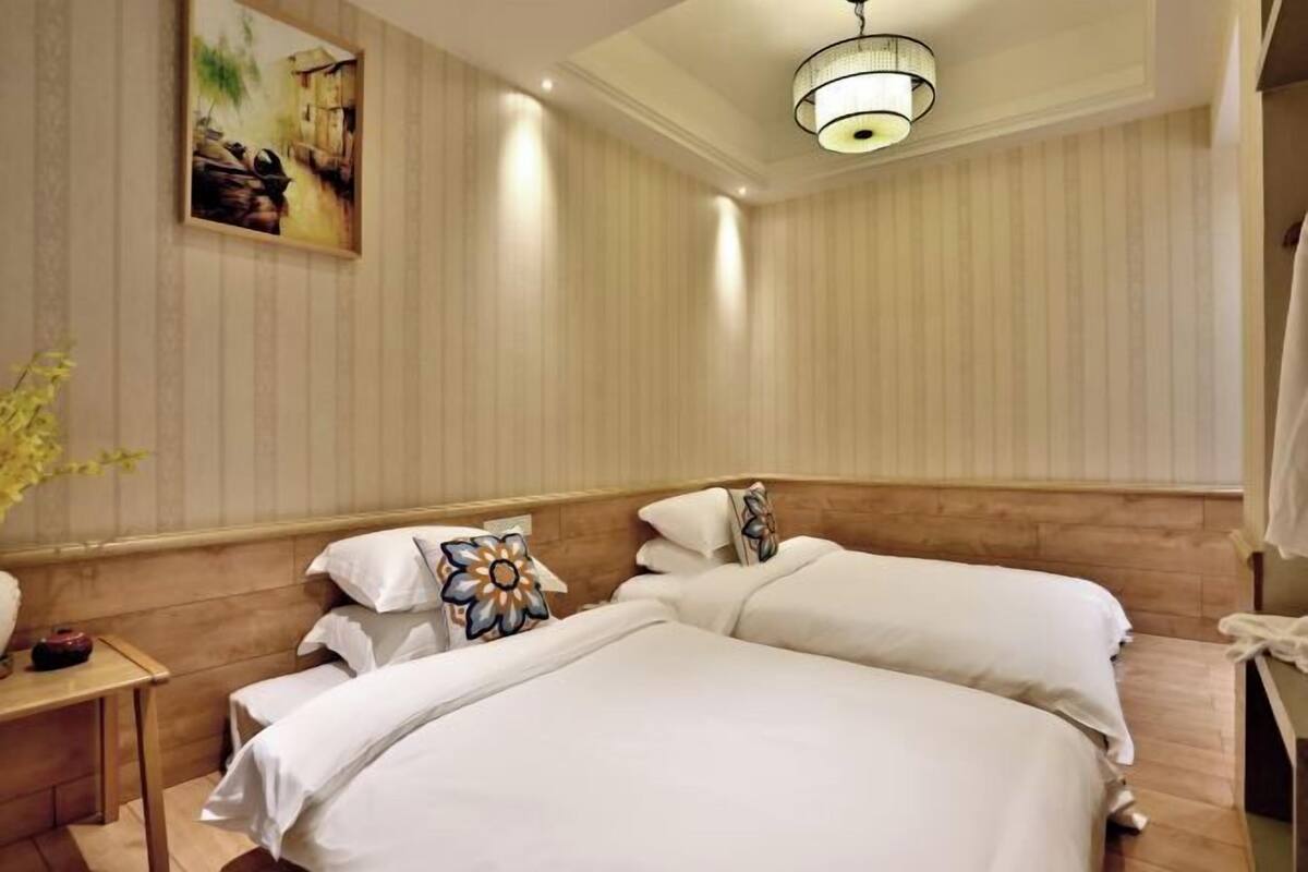 A hotel room with two beds, a wooden headboard, a painting on the wall, a bedside table with a lamp, and a wooden floor.