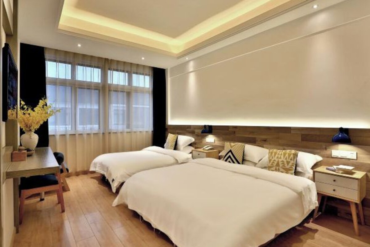 Habitación de hotel con dos camas, un escritorio, una silla, una mesita de noche y un ventanal con cortinas.