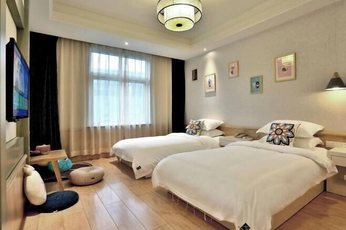 A hotel room with two beds, a TV, a desk, and a window with curtains.