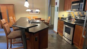 A compact kitchen with a central island, wooden cabinets, a microwave, an oven, and a sink.