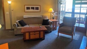 A living room with a sofa, armchair, and a coffee table. There is a lamp on a side table and a framed picture on the wall.