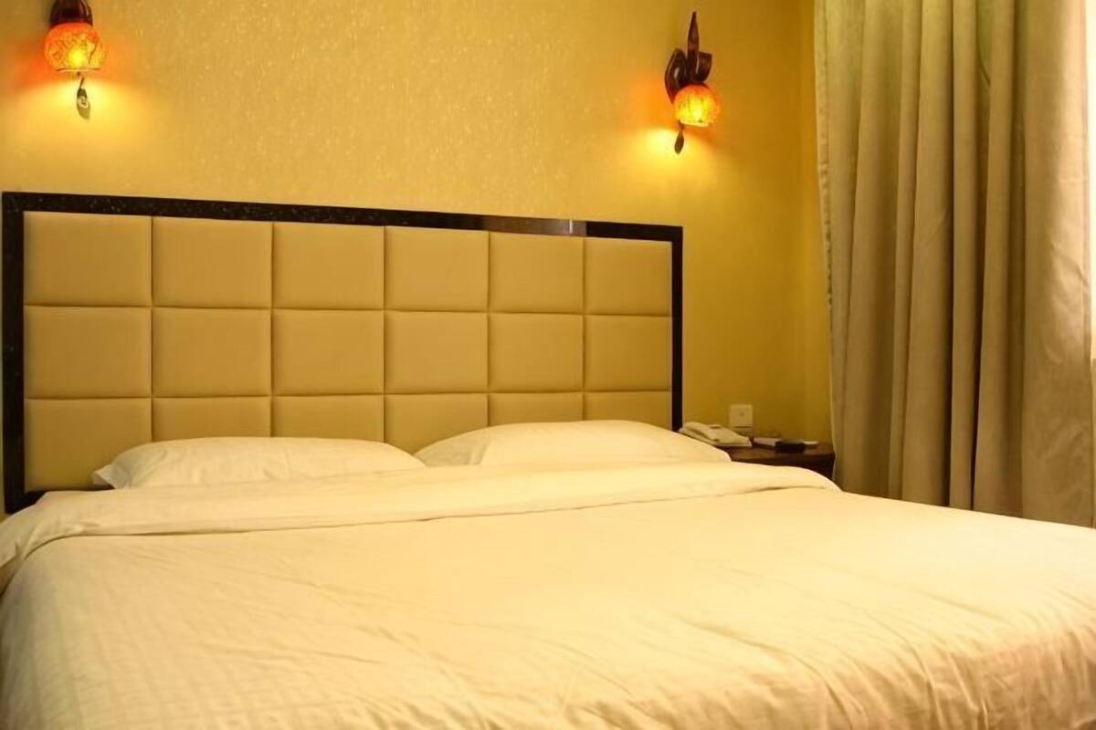 Een bed met hoofdeinde, twee bedlampjes en een gordijn.