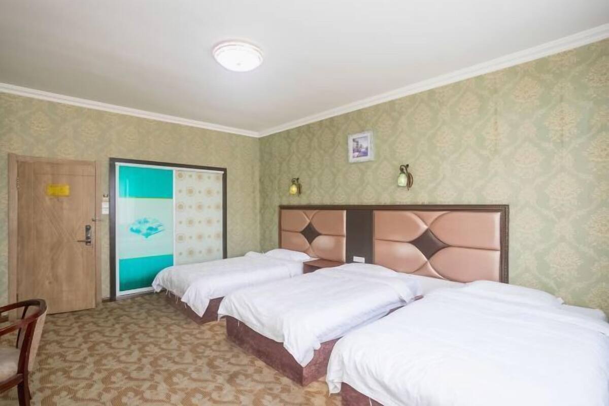 Een hotelkamer met drie bedden, een houten deur en behang met een patroon.