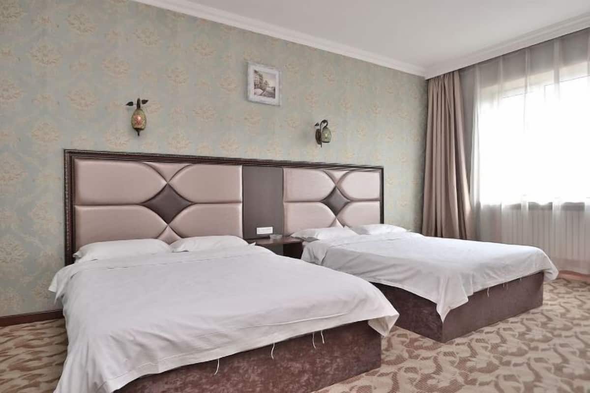 Hotelkamer met twee bedden, een groot hoofdeinde, een nachtkastje en een raam met gordijnen.