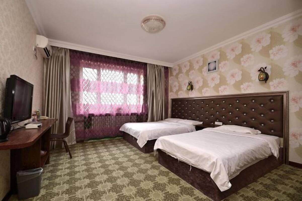 Een hotelkamer met twee bedden, een bureau met televisie en een raam met gordijnen.