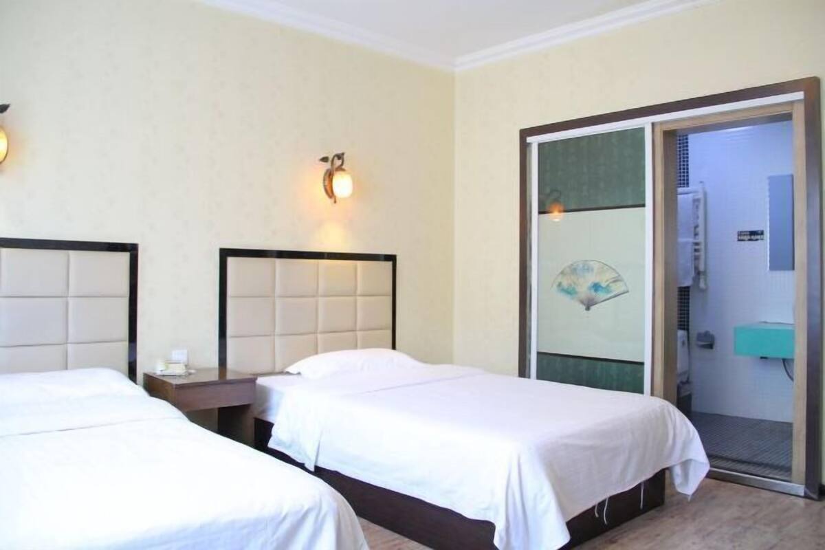 Een hotelkamer met twee bedden, een nachtkastje, een aan de muur bevestigd lampje, en een badkamer die zichtbaar is door een glazen deur.