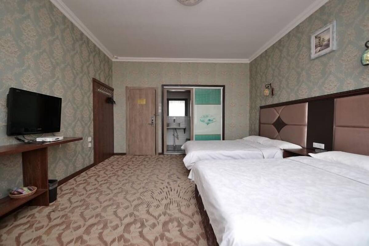 Een hotelkamer met twee bedden, een televisie op een standaard, een kledingkast en een deur naar een badkamer.