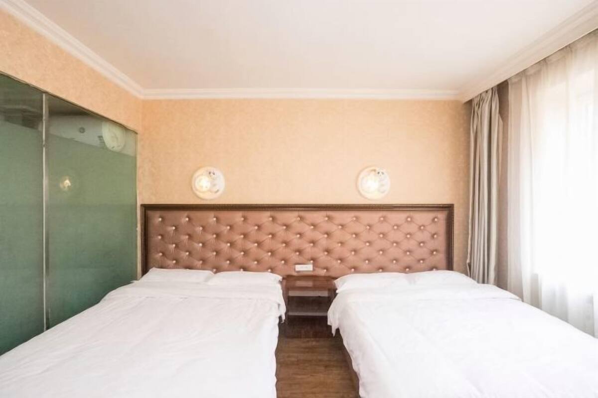 Een hotelkamer met twee bedden, een gestoffeerd hoofdeinde, een spiegel en een raam met gordijnen.