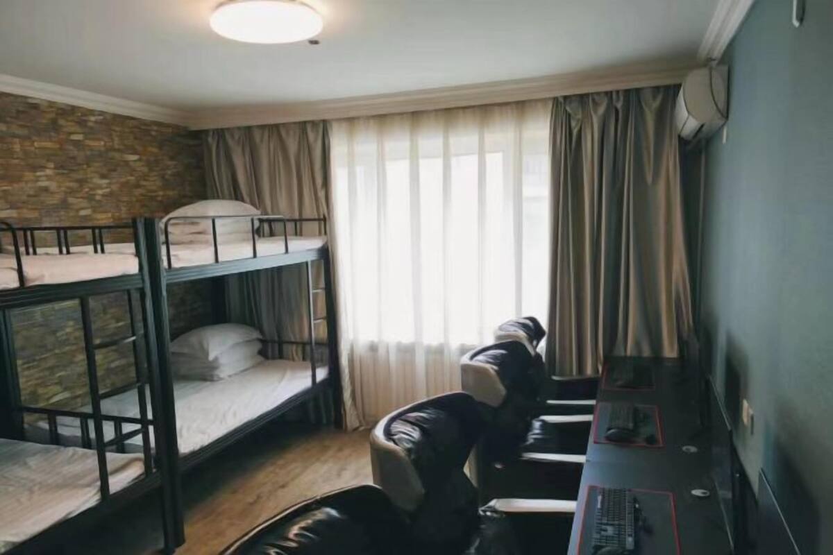 Een slaapkamer met stapelbed, bureau en stoel, een raam met gordijnen en een stenen muur.