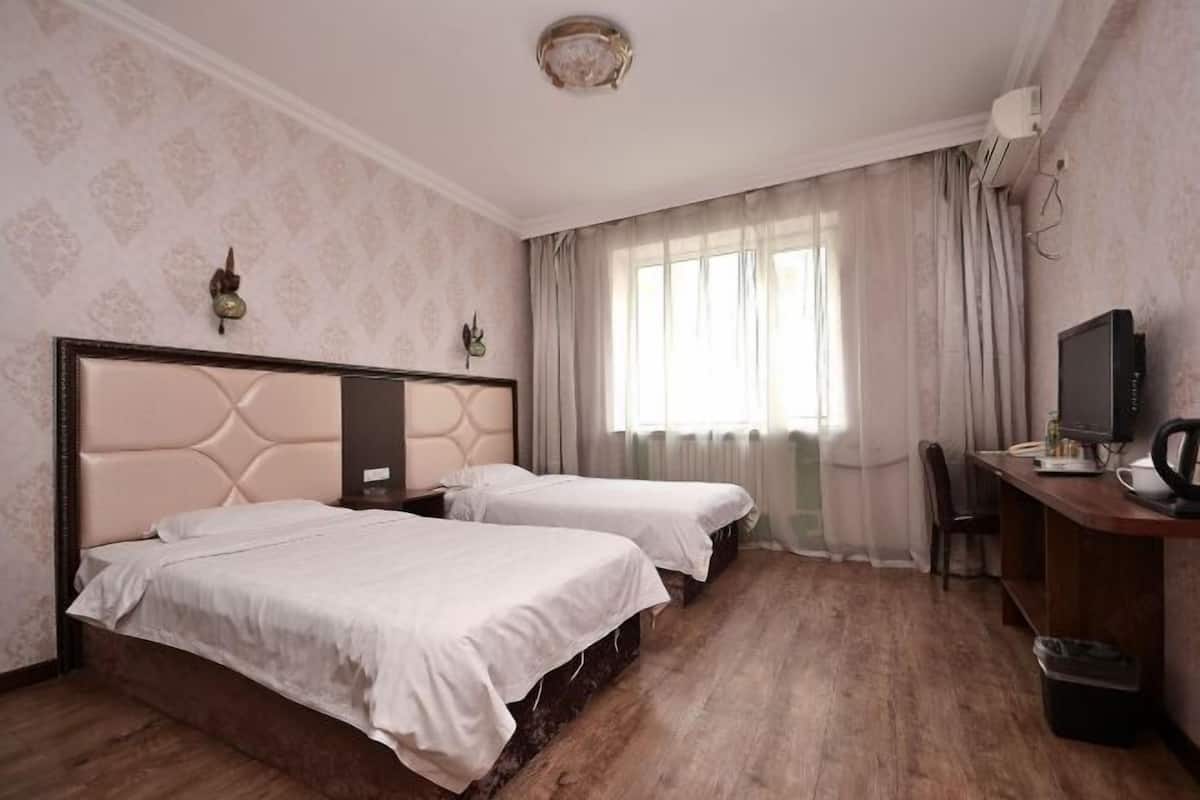 Een hotelkamer met twee bedden, een bureau met een computer, een stoel en een raam met gordijnen.
