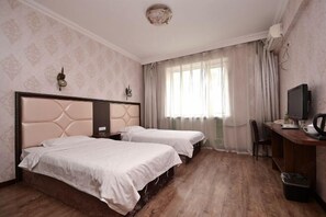 Ein Hotelzimmer mit zwei Betten, einem Schreibtisch mit Computer, einem Stuhl und einem Fenster mit Vorhängen.
