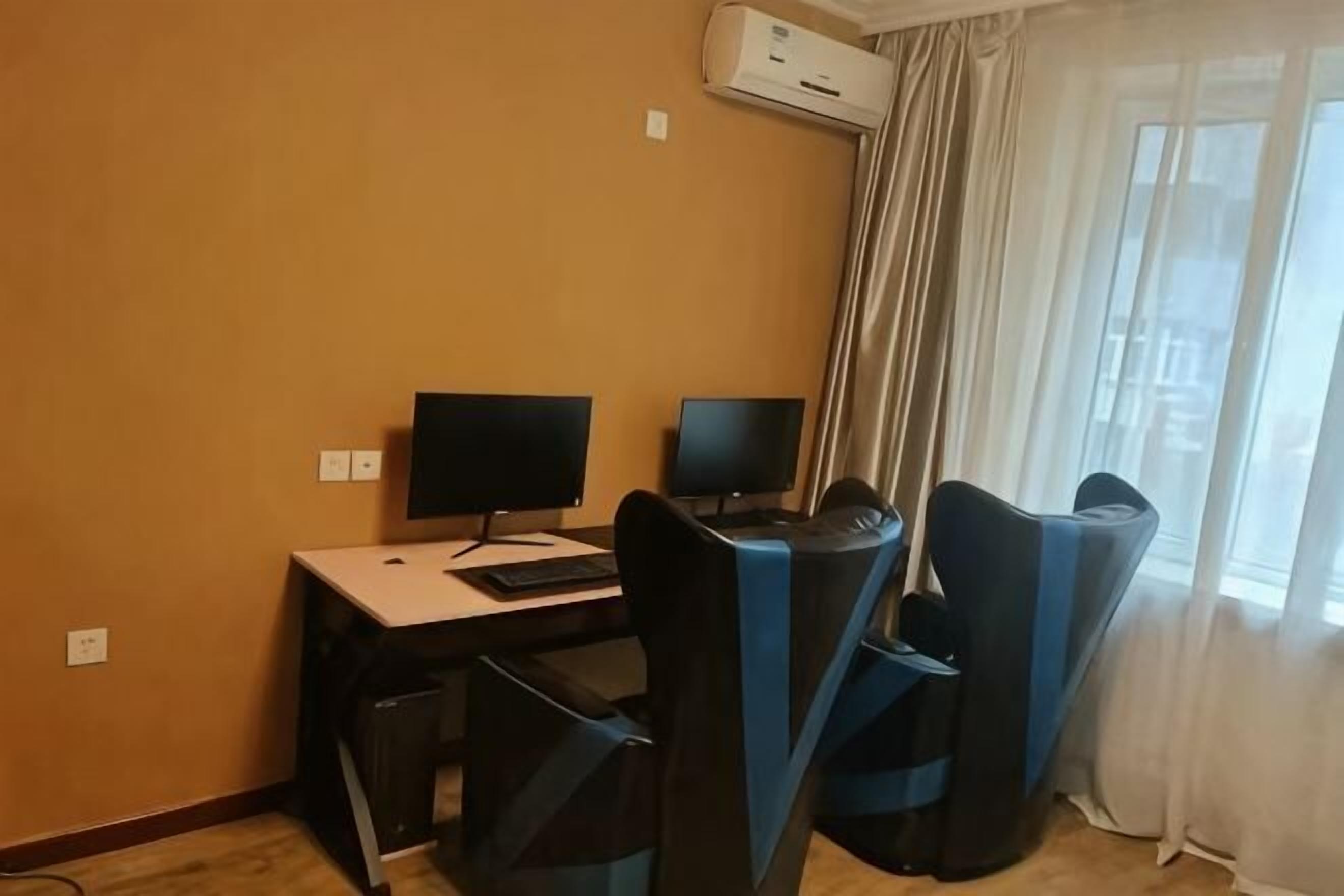 Una habitación con escritorio, dos monitores, una silla y un aire acondicionado.
