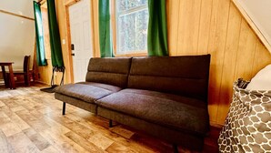 A cozy room with a sofa, wooden flooring, a window with curtains, and a patterned chair.
