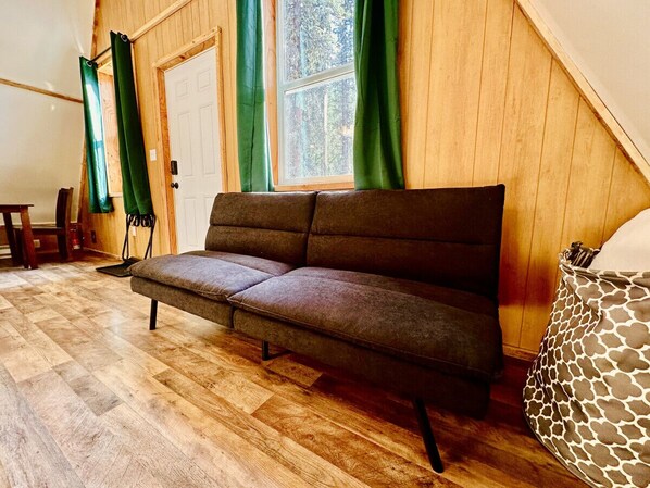 A cozy room with a sofa, wooden flooring, a window with curtains, and a patterned chair. - Roberts Lodge in Tok, Alaska (Tok)