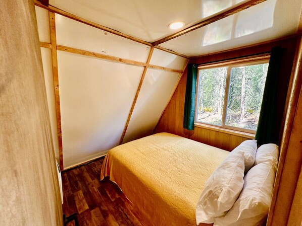 Un dormitorio pequeño y acogedor con una cama individual, paredes de madera y una ventana que ofrece vistas a árboles.