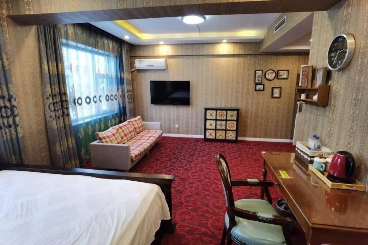 A hotel room with a bed, a sofa, a desk, a chair, a TV, and a red carpet.