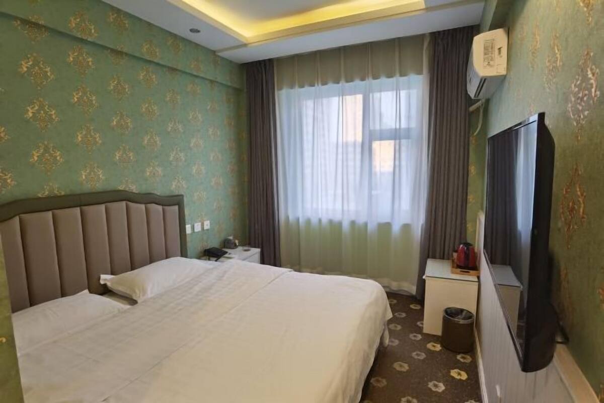 A hotel room with a bed, a nightstand, a TV, and a window with curtains.