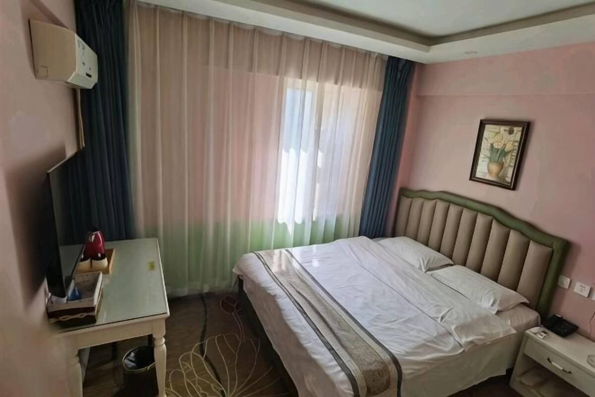 A hotel room with a bed, bedside table, lamp, and a window with curtains.