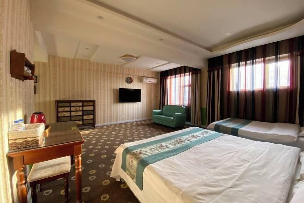 A hotel room with two beds, a desk, a chair, a television, and a window with curtains.