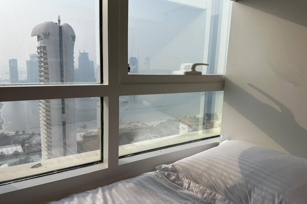 A hotel room with a large window, a bed, and a view of a cityscape with tall buildings.
