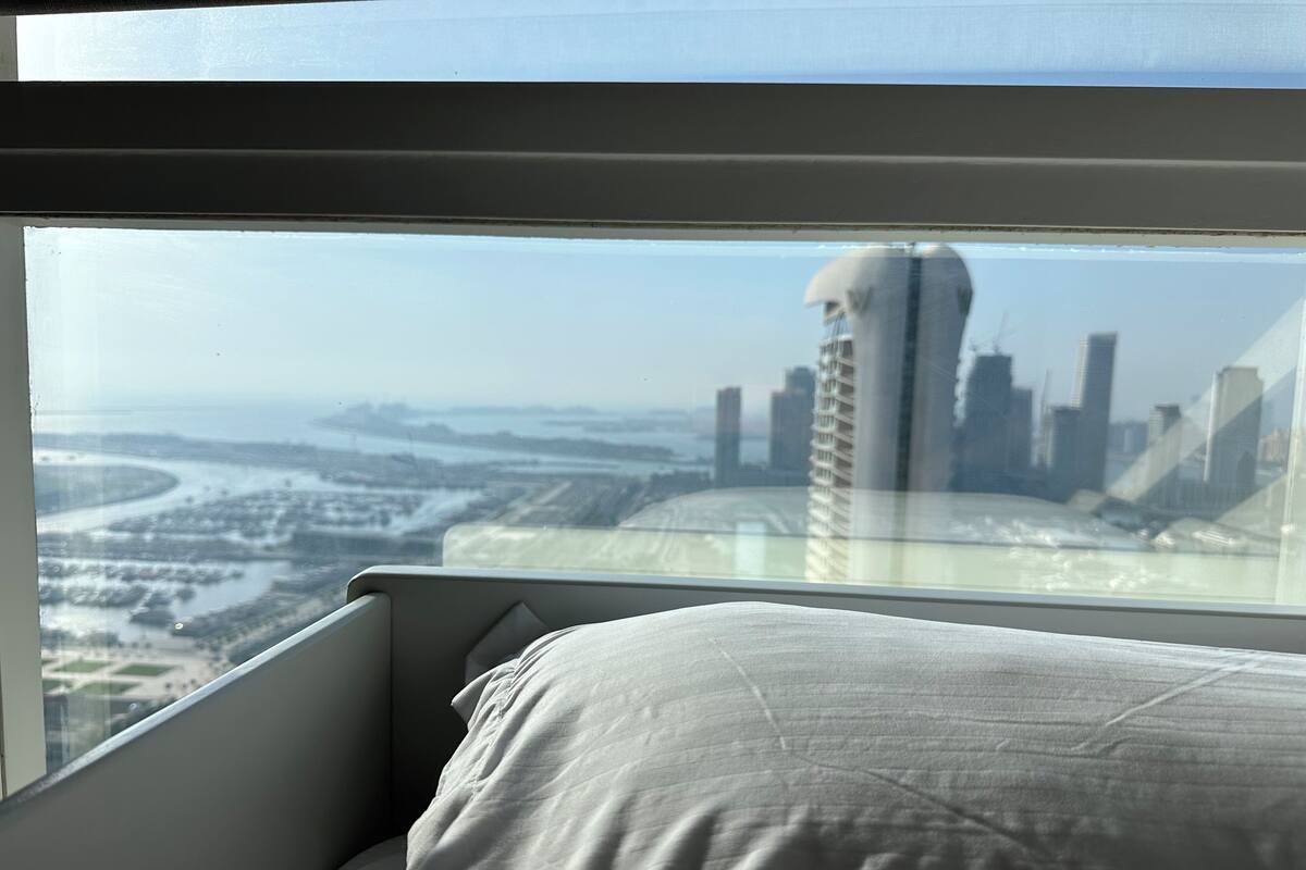A bed with a view of a cityscape through a window.