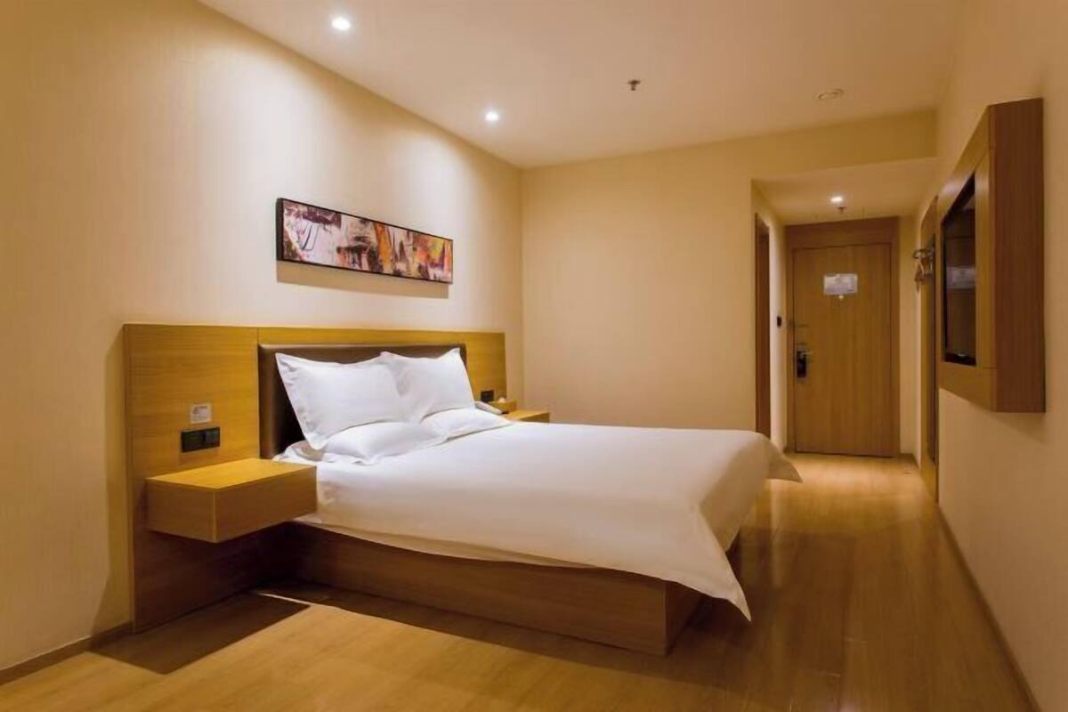 A hotel room with a bed, bedside tables, a wall-mounted artwork, and a wooden door.